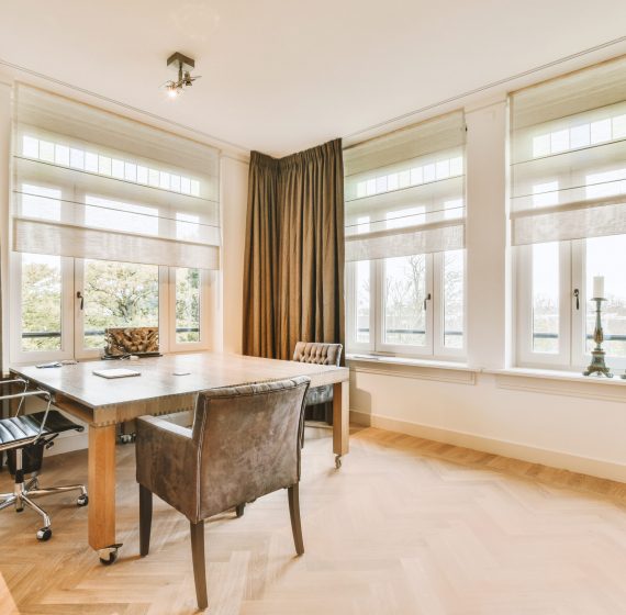 a home office with a desk and three windows a home office area with wood flooring and large windows that look out onto the street in front of the house
